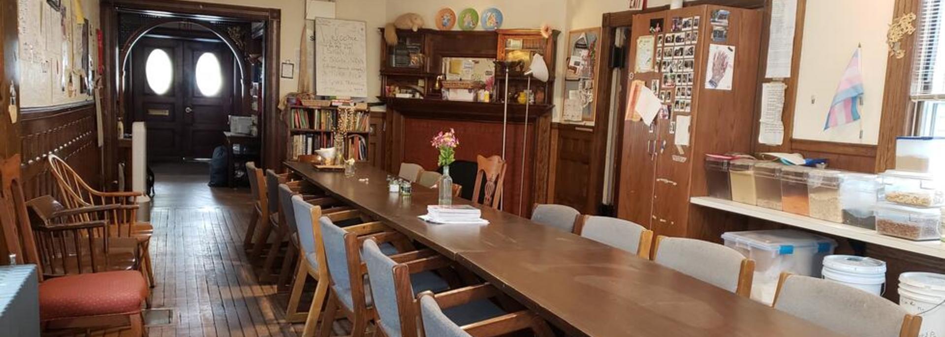 Dudley Co-op dining room showing long dining table with many chairs, flowers and books on the table, and a view of the front door.